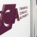 A wall with a large maroon Financial Conduct Authority (FCA) logo and text, next to a modern hallway with white walls and ceiling lights.