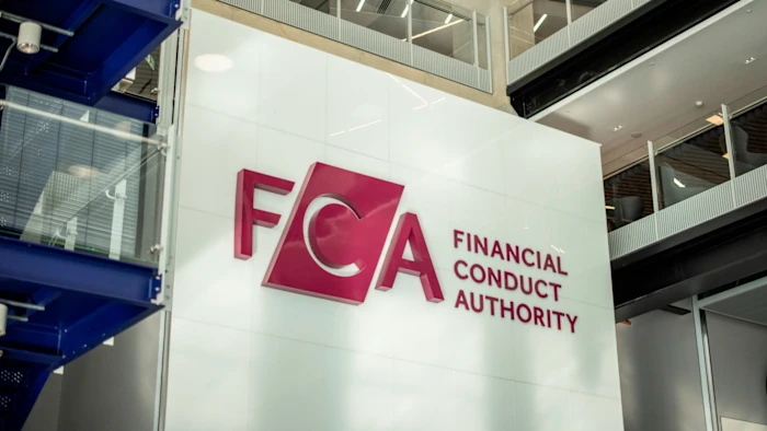 The logo and name of the Financial Conduct Authority (FCA) are displayed on a large white wall inside a modern office building with glass and metal features, reflecting its oversight roles in sectors such as Crypto UK.