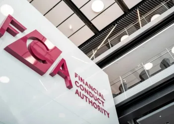 Large red letters spelling “FCA” and “Financial Conduct Authority” are displayed on a modern white wall inside an office building, reflecting the FCA’s oversight of Crypto UK markets, with balconies and ceiling lights visible above.