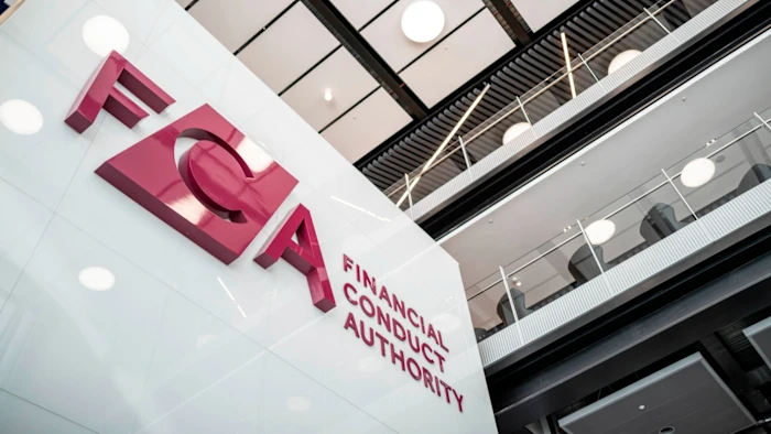 Large red letters spelling “FCA” and “Financial Conduct Authority” are displayed on a modern white wall inside an office building, reflecting the FCA’s oversight of Crypto UK markets, with balconies and ceiling lights visible above.