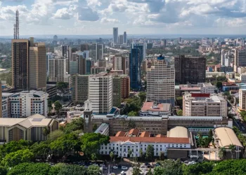 Aerial view of Nairobi’s city center, featuring tall modern skyscrapers, various office buildings, and lush green areas under a partly cloudy sky.