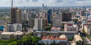 Aerial view of Nairobi’s city center, featuring tall modern skyscrapers, various office buildings, and lush green areas under a partly cloudy sky.